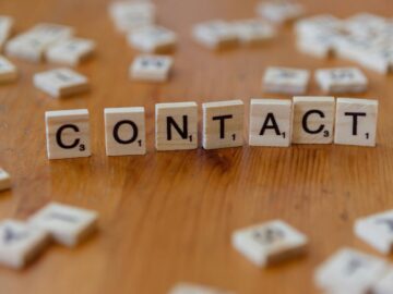 Scrabble letters spelling 'contact' on a wooden table surface.