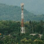 Cellular tower surrounded by lush tropical greenery with mountains in the background.