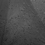 Detailed close-up of raindrops on a black umbrella, showcasing texture and water droplets.