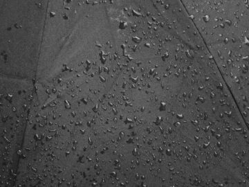 Detailed close-up of raindrops on a black umbrella, showcasing texture and water droplets.