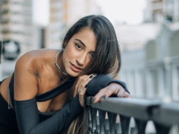 Portrait of a stylish woman leaning on a balcony railing with cityscape background.