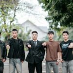 Six young adults standing outdoors, demonstrating unity with outstretched fists.