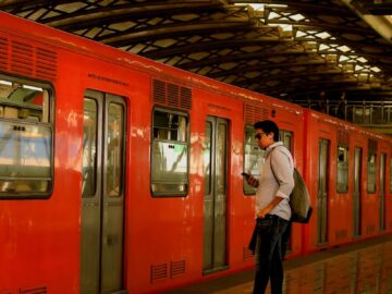 Man holding phone on metro platform beside a brightly colored train.