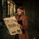 Stylish man reading The New York Times in a city alleyway during sunset.