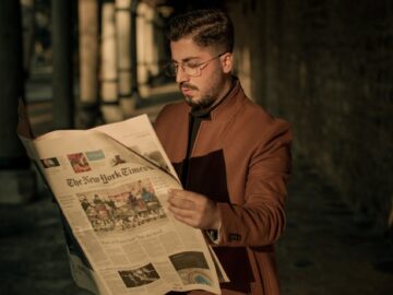 Stylish man reading The New York Times in a city alleyway during sunset.