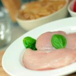 Close-up of raw chicken breasts on a plate with basil leaves, ideal for culinary themes.