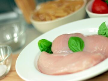 Close-up of raw chicken breasts on a plate with basil leaves, ideal for culinary themes.