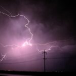 Stunning lightning bolts illuminate a stormy night sky over silhouetted power lines.