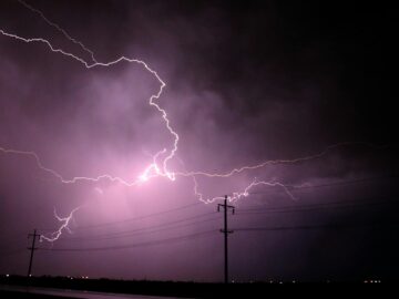 Stunning lightning bolts illuminate a stormy night sky over silhouetted power lines.