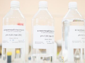 Clear bottles of buffer solution with pH labels in a laboratory setting.