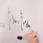 Person writing math equations on a whiteboard, focusing on integrals and formulas.