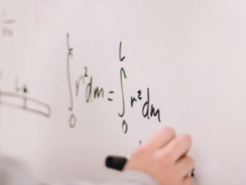 Person writing math equations on a whiteboard, focusing on integrals and formulas.