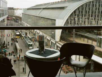 View from contemporary cafeteria with cozy chairs and small round table near fence in front of construction exterior and people walking on street in town