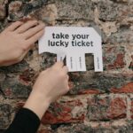 Close-up of hands pulling a lucky ticket from paper on a rustic brick wall.