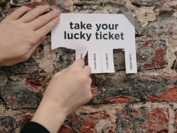 Close-up of hands pulling a lucky ticket from paper on a rustic brick wall.