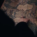 A person examining a detailed vintage map in a dimly lit environment, evoking curiosity and adventure.