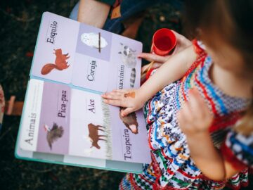 Young girl reading a colorful animal picture book outdoors, enjoying a sunny day in the park.