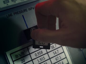 Close-up of hand adjusting pressure gauge dial in an industrial setting with visible pressure readings and controls.