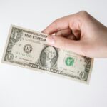 Close-up of a Caucasian hand holding a US one dollar bill against a white background.