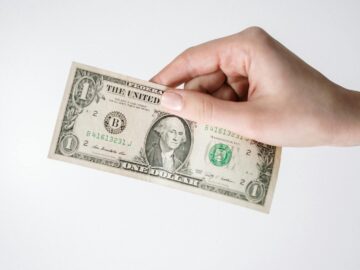 Close-up of a Caucasian hand holding a US one dollar bill against a white background.