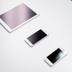 Overhead view of a digital tablet, smartphone, and stylus on a white surface.