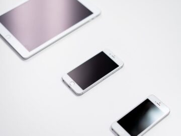 Overhead view of a digital tablet, smartphone, and stylus on a white surface.