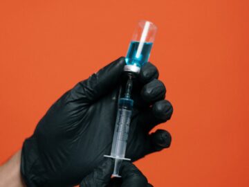 Close-up of hands with black gloves preparing a syringe against orange background.