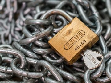A detailed macro shot of a brass padlock with a key on heavy steel chains, symbolizing security and protection.