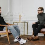 Teen boy in a hoodie having a conversation with a therapist in a stylish, minimalist room setting.