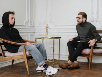 Teen boy in a hoodie having a conversation with a therapist in a stylish, minimalist room setting.