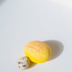 A bright yellow Easter egg and speckled quail egg on a white background in soft light.