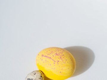 A bright yellow Easter egg and speckled quail egg on a white background in soft light.