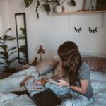 Woman enjoying remote work from home with laptop in a cozy bedroom.