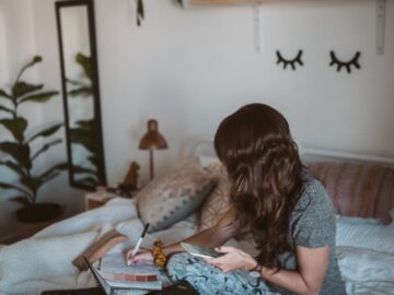 Woman enjoying remote work from home with laptop in a cozy bedroom.