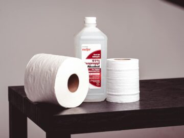 Close-up of isopropyl alcohol bottle and tissue rolls on a wooden table, emphasizing hygiene.