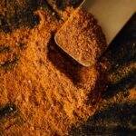From above of pile of multicolored mix of curcuma and powdered peppers on black surface and wooden spatula