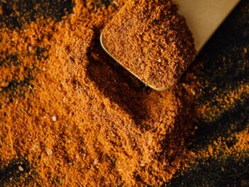 From above of pile of multicolored mix of curcuma and powdered peppers on black surface and wooden spatula