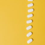 Top view composition of white medical pills placed in row vertically on vivid yellow background