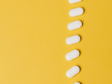 Top view composition of white medical pills placed in row vertically on vivid yellow background