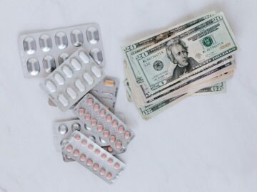 Blister packs of pills and US dollars on a white surface.