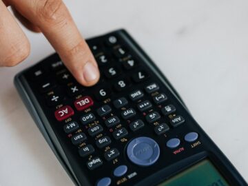 From above of crop anonymous economist calculating on calculator with plastic buttons while making budget on marble table