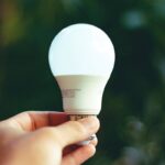 Close-up of a hand holding a glowing LED bulb outdoors, symbolizing innovation and eco-friendly energy.