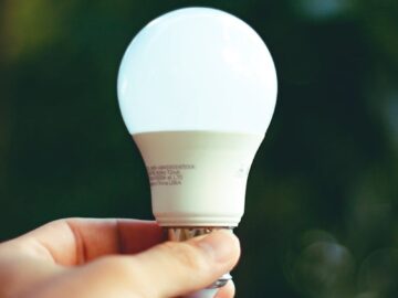 Close-up of a hand holding a glowing LED bulb outdoors, symbolizing innovation and eco-friendly energy.