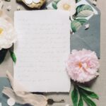 A beautifully arranged vintage letter surrounded by a pink peony, key, and floral envelope, creating a soft, romantic ambiance.