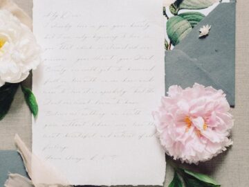 A beautifully arranged vintage letter surrounded by a pink peony, key, and floral envelope, creating a soft, romantic ambiance.