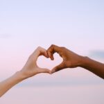 A powerful image of unity and diversity with two hands forming a heart against a serene pastel sky.