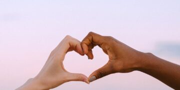 A powerful image of unity and diversity with two hands forming a heart against a serene pastel sky.
