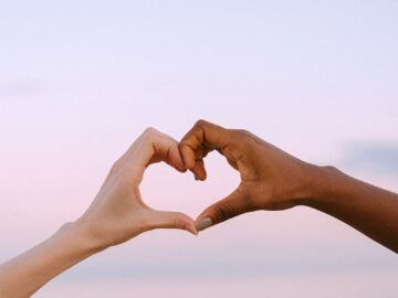 A powerful image of unity and diversity with two hands forming a heart against a serene pastel sky.