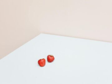 A clean and minimalist shot of two fresh strawberries on a white table.