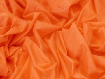 A detailed close-up of rippled orange textile fabric, ideal for use as a vibrant background or design element.